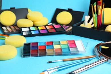 Photo of Bright face paints, brushes, mirror and sponges on light blue background