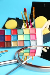 Photo of Bright face paints, brushes, mirror and sponges on light blue background, closeup