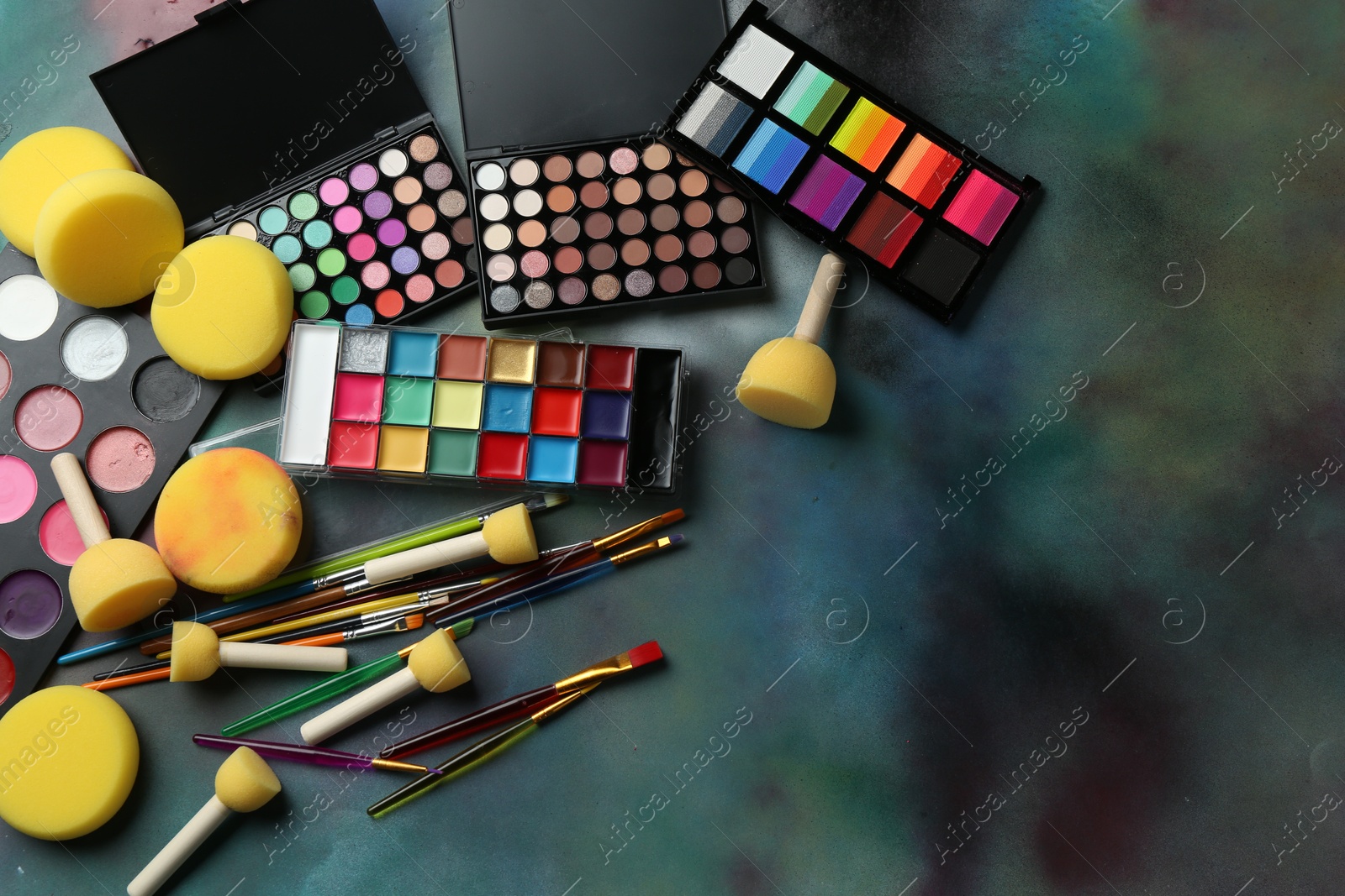 Photo of Bright face paints, brushes and sponges on color background, flat lay. Space for text