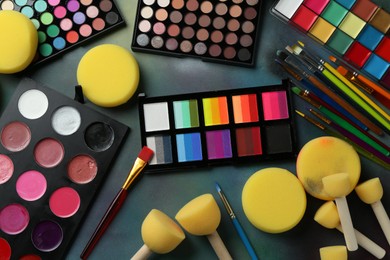 Photo of Bright face paints, brushes and sponges on color background, flat lay