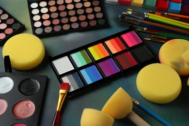 Photo of Bright face paints, brushes and sponges on color background