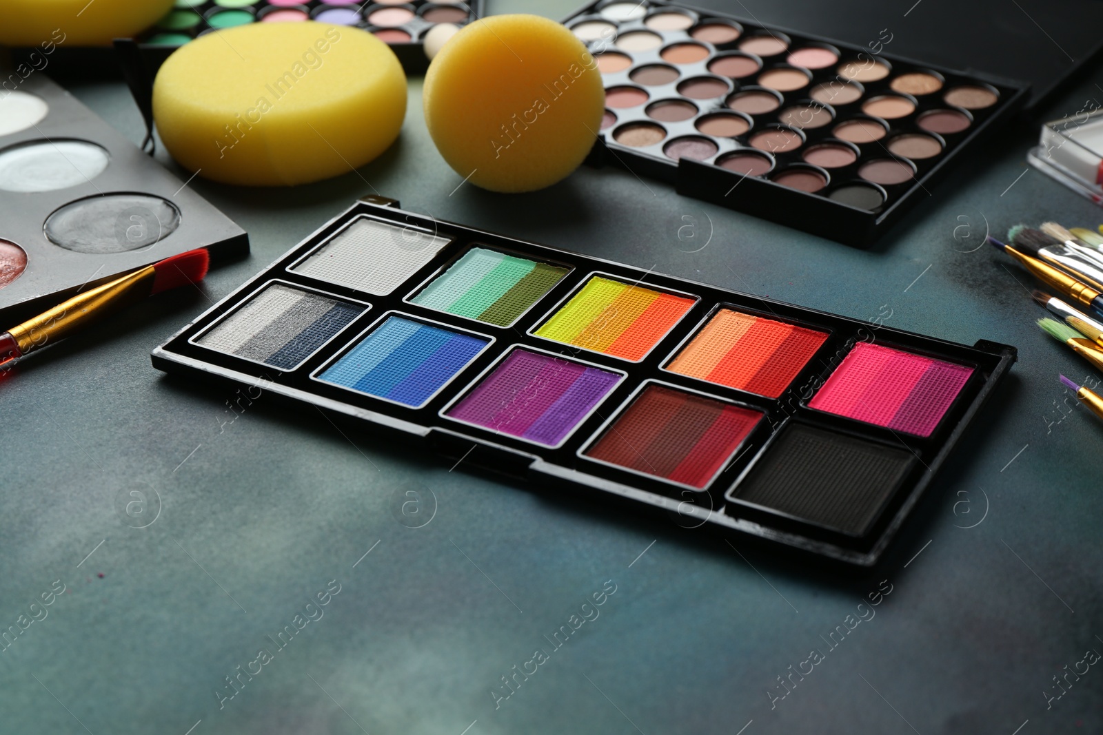 Photo of Bright face paints, brushes and sponges on color background, closeup