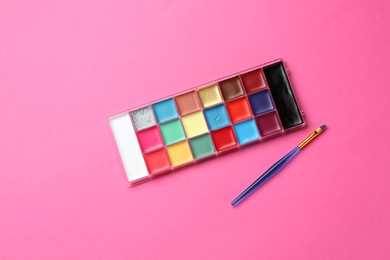 Photo of Bright face paints and brush on pink background, top view