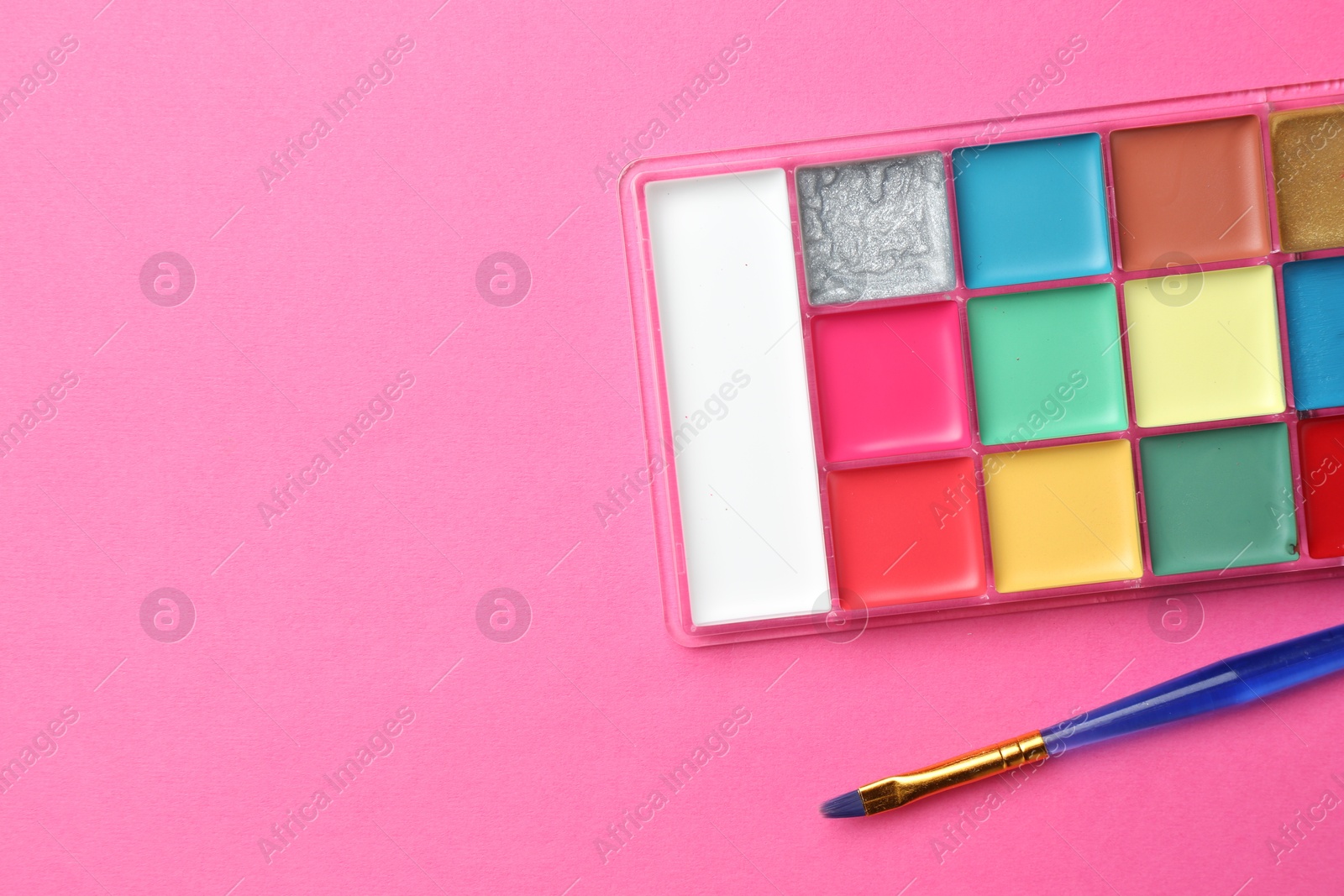 Photo of Bright face paints and brush on pink background, top view. Space for text