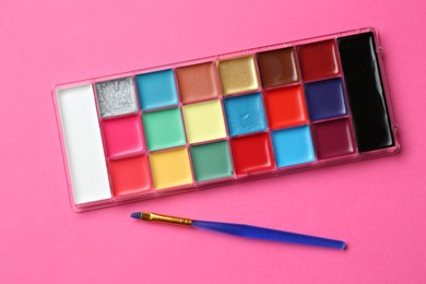 Photo of Bright face paints and brush on pink background, top view