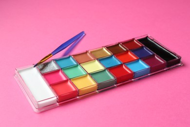 Photo of Bright face paints and brush on pink background