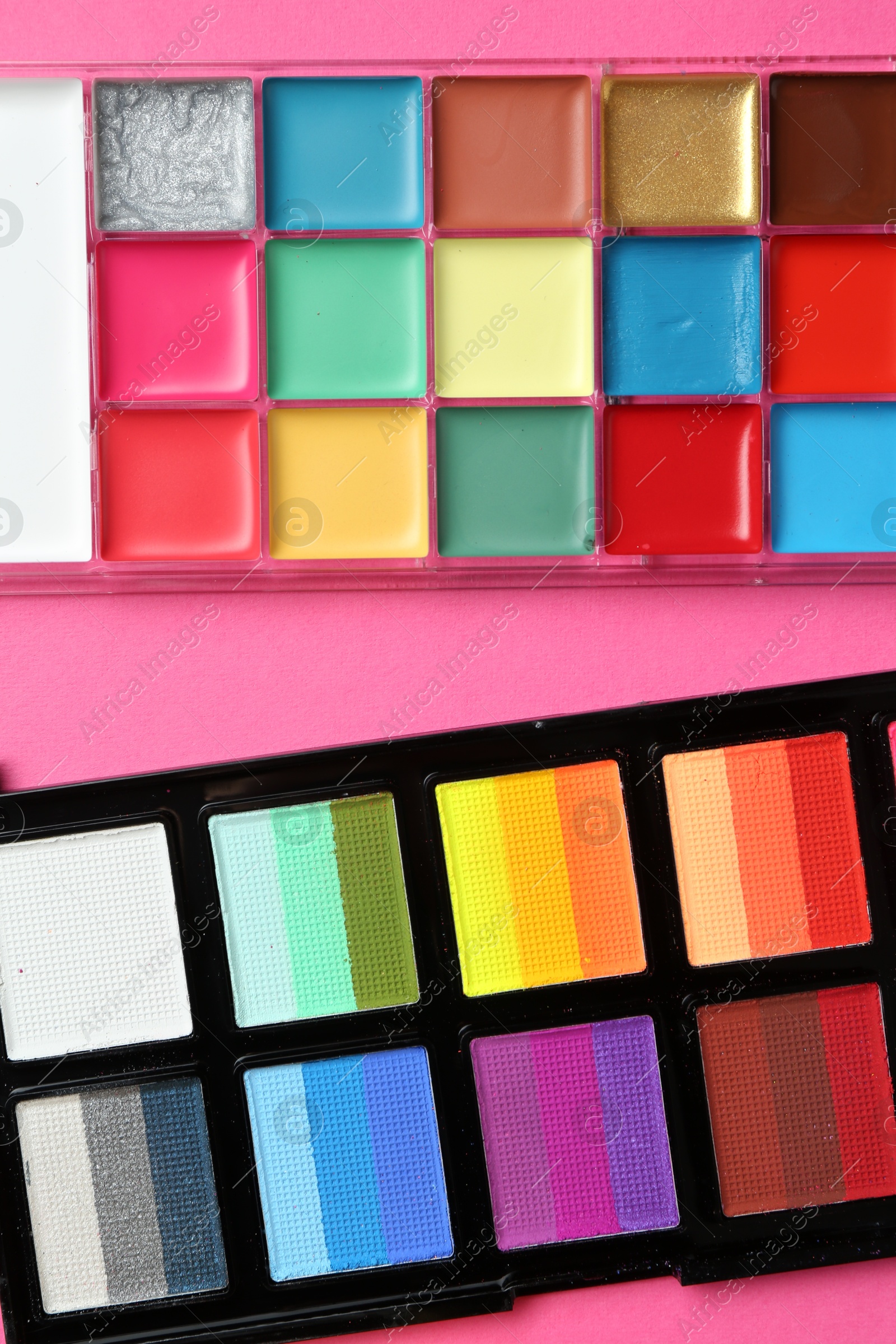 Photo of Bright face paints on pink background, top view