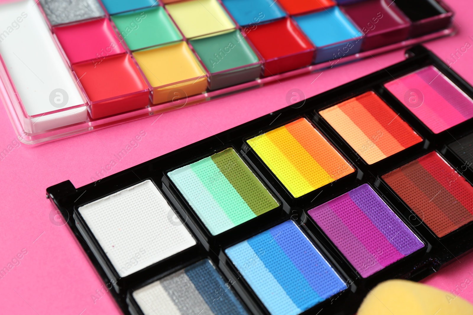 Photo of Bright face paints and sponge on pink background, closeup