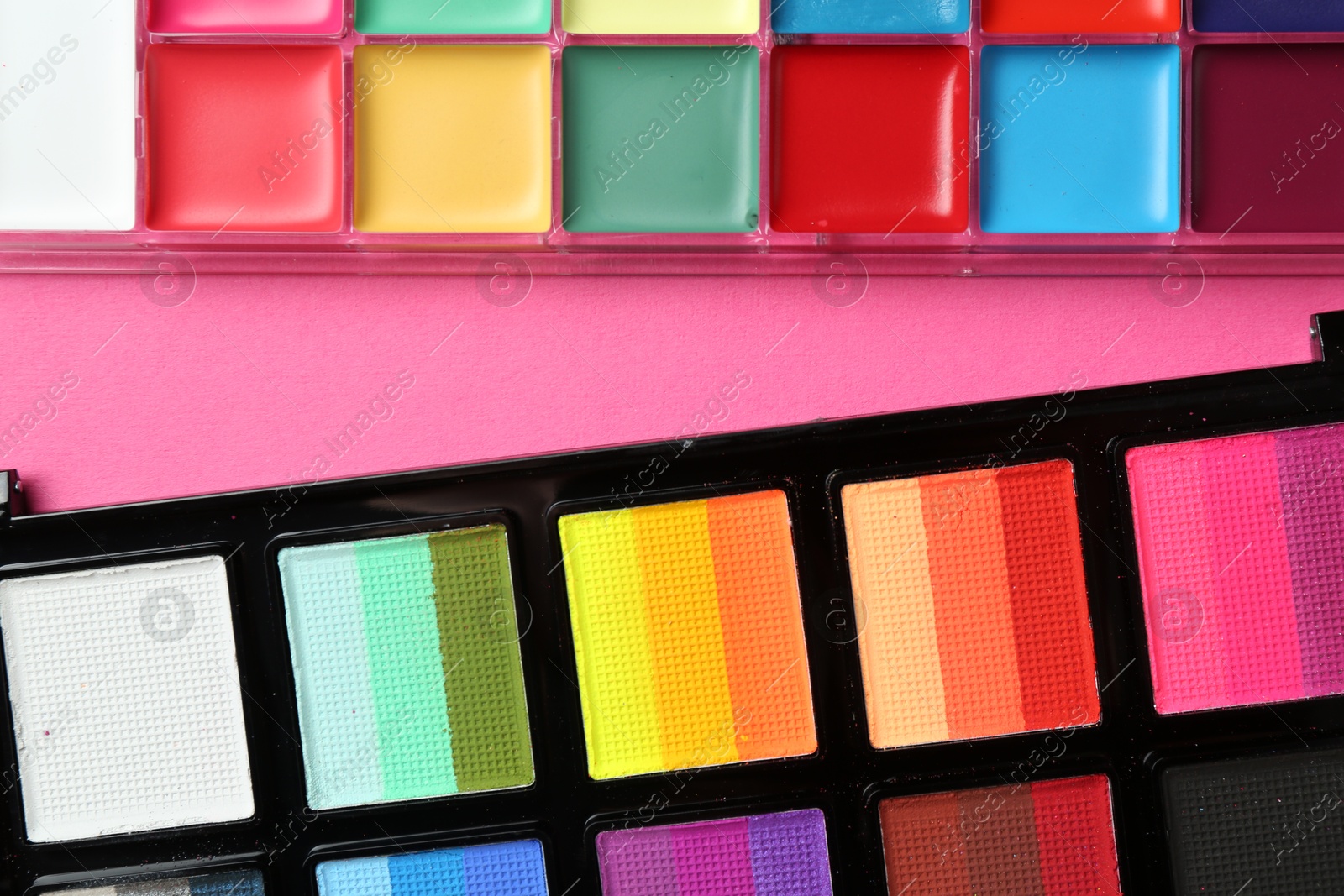 Photo of Bright face paints on pink background, top view