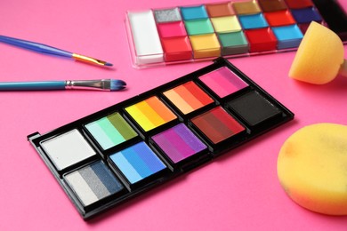 Photo of Bright face paints, brushes and sponges on pink background, closeup