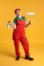 Photo of Professional painter with roller and bucket of paint on orange background