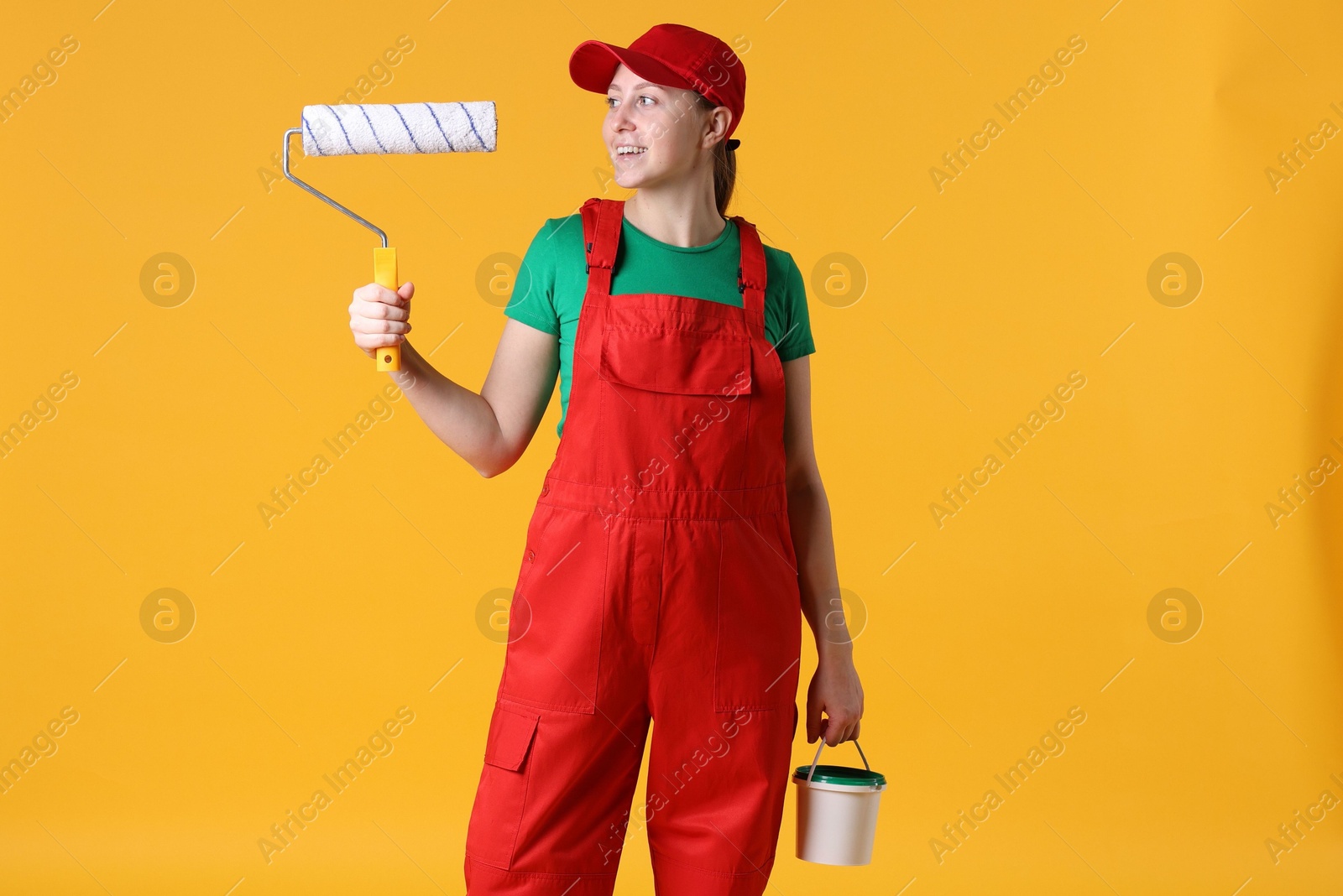 Photo of Professional painter with roller and bucket of paint on orange background