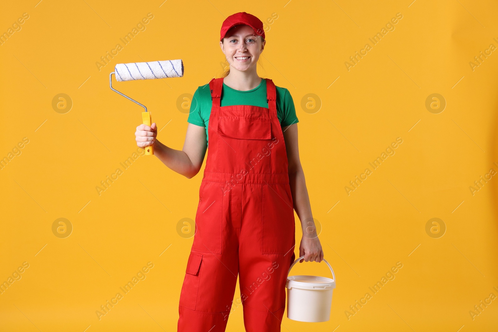 Photo of Professional painter with roller and bucket of paint on orange background