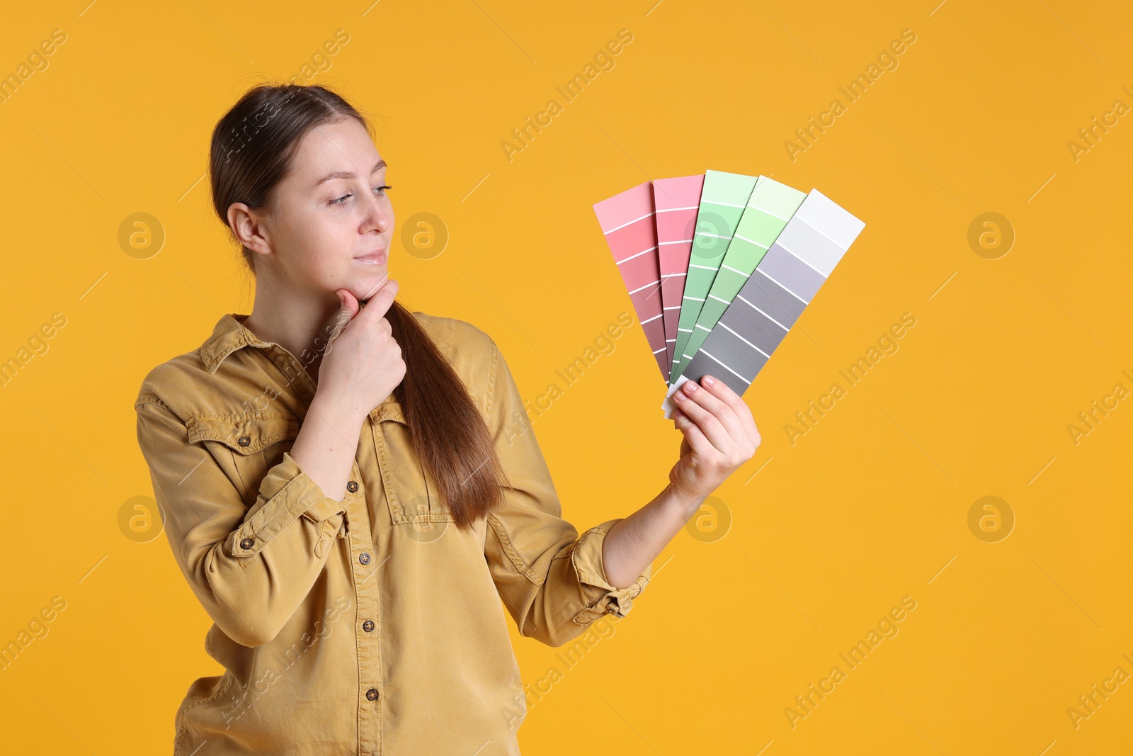 Photo of Woman with paint color selection chart on orange background