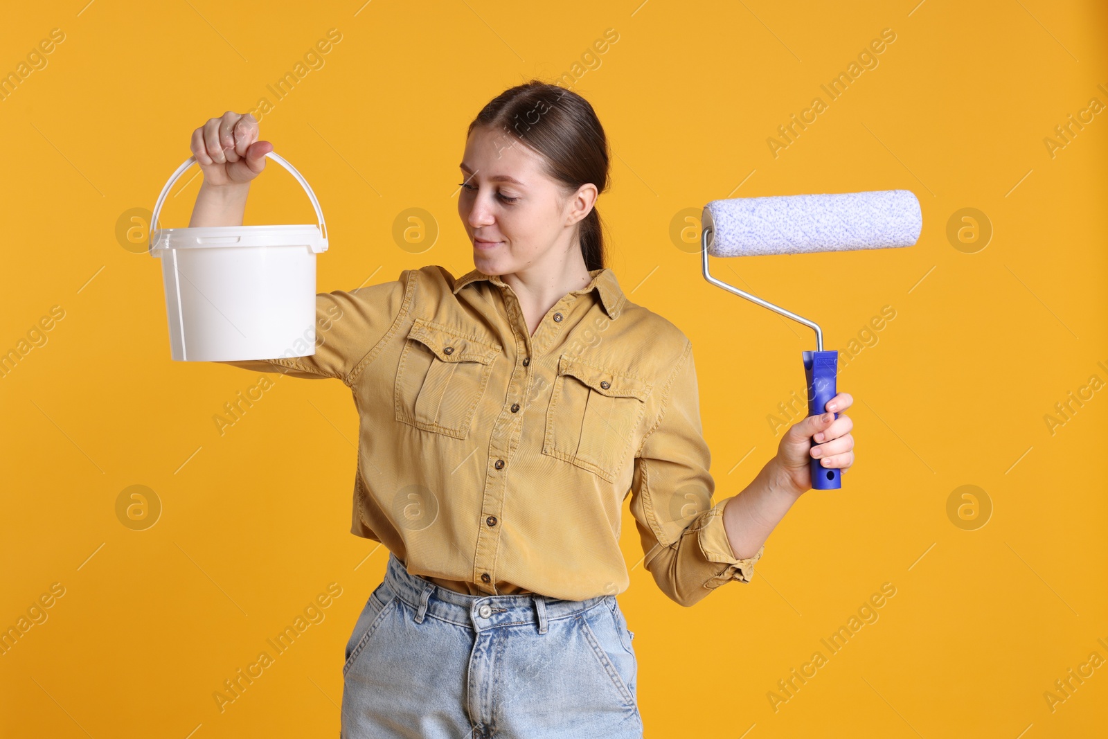 Photo of Woman with roller and bucket of paint on orange background