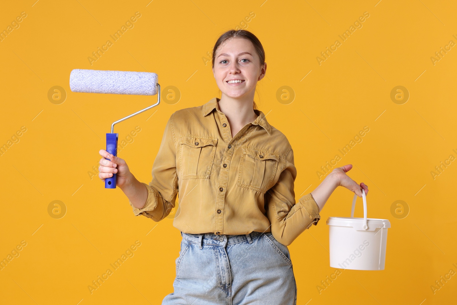 Photo of Woman with roller and bucket of paint on orange background