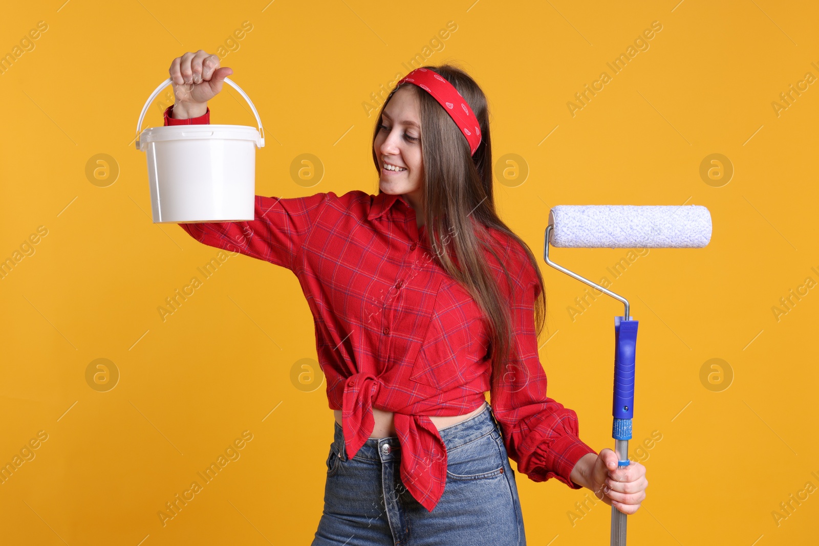 Photo of Woman with roller and bucket of paint on orange background