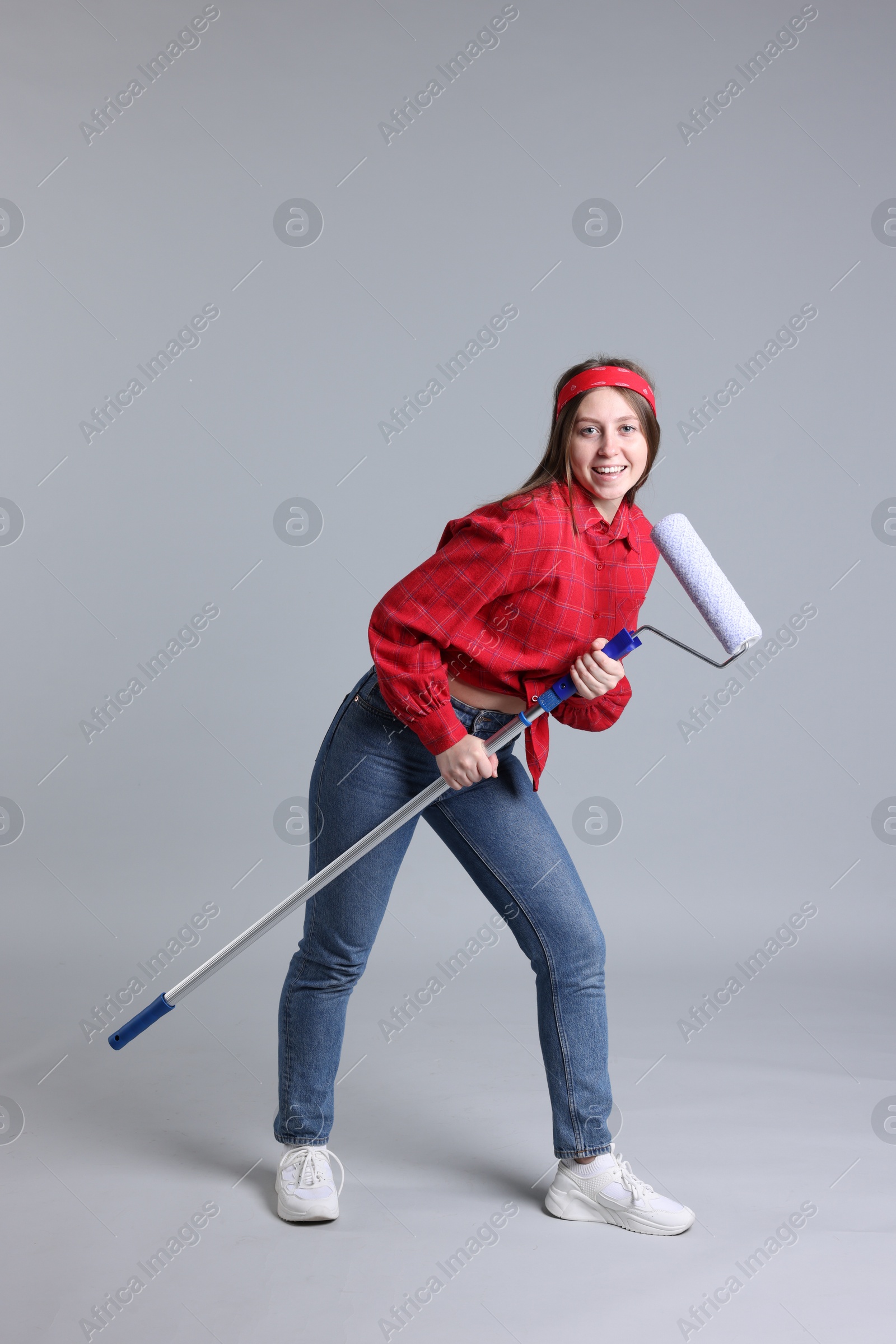 Photo of Woman with paint roller having fun on light grey background