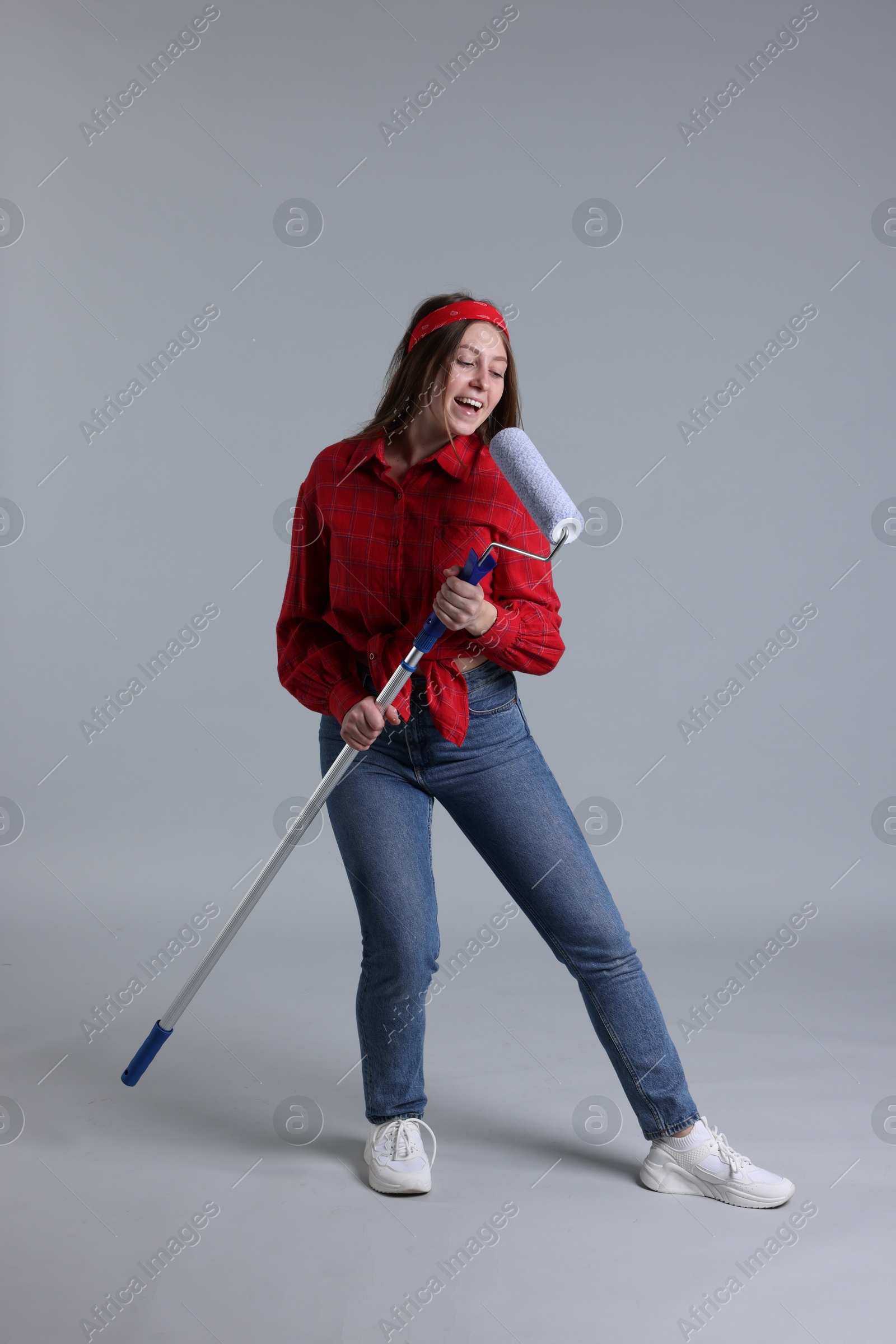 Photo of Woman with paint roller having fun on light grey background