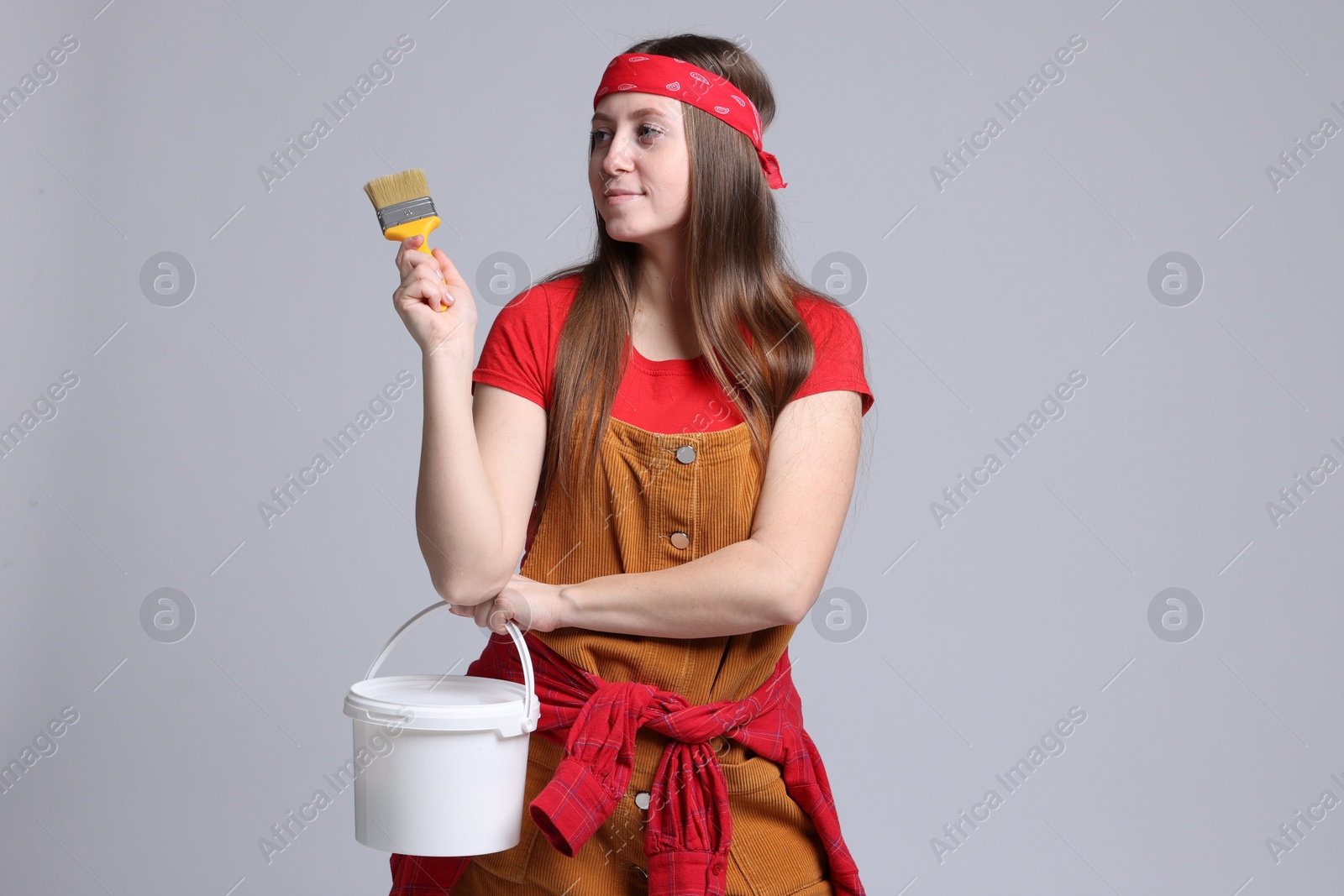 Photo of Woman with brush and bucket of paint on light grey background