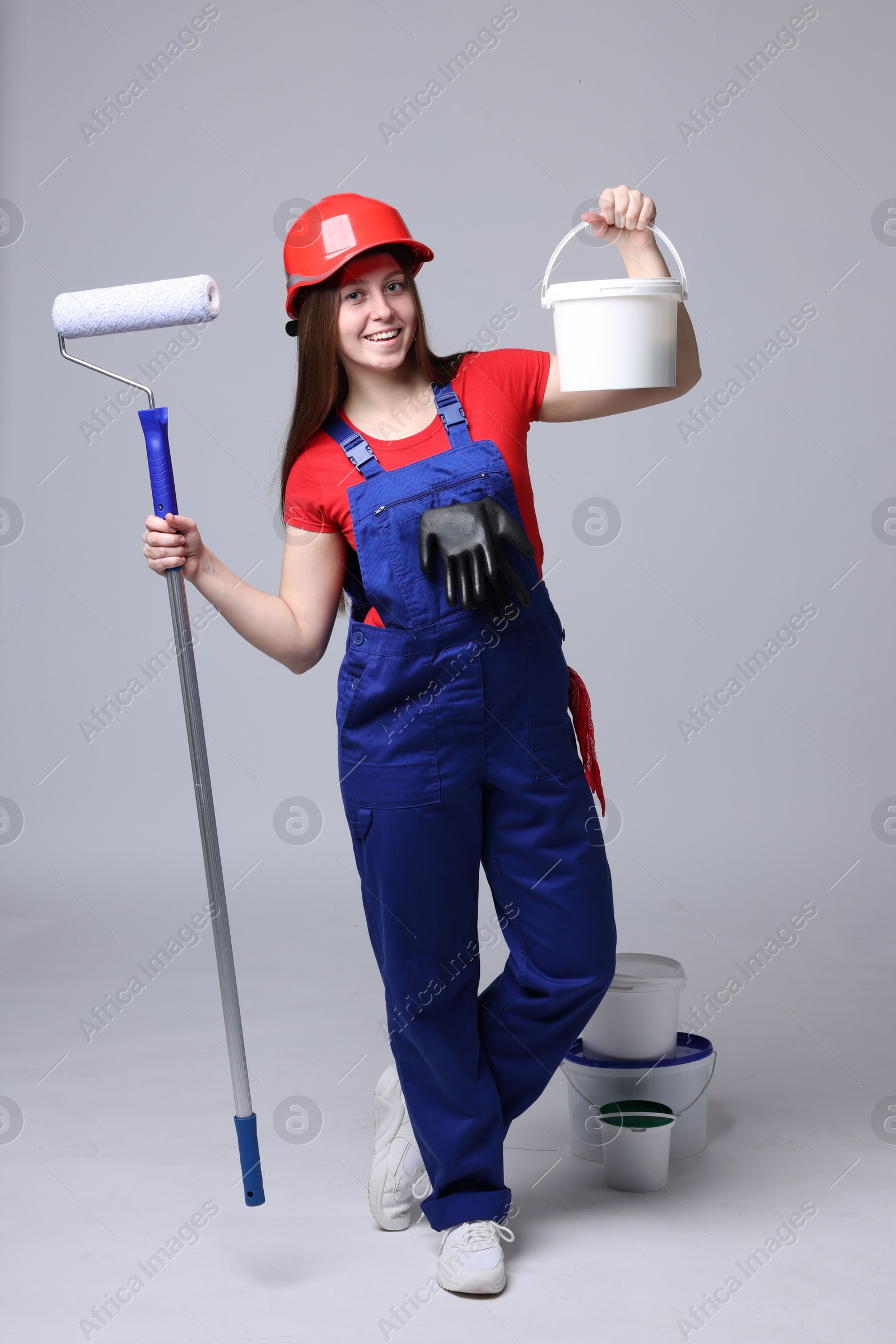 Photo of Professional painter with roller and buckets of paint on light grey background