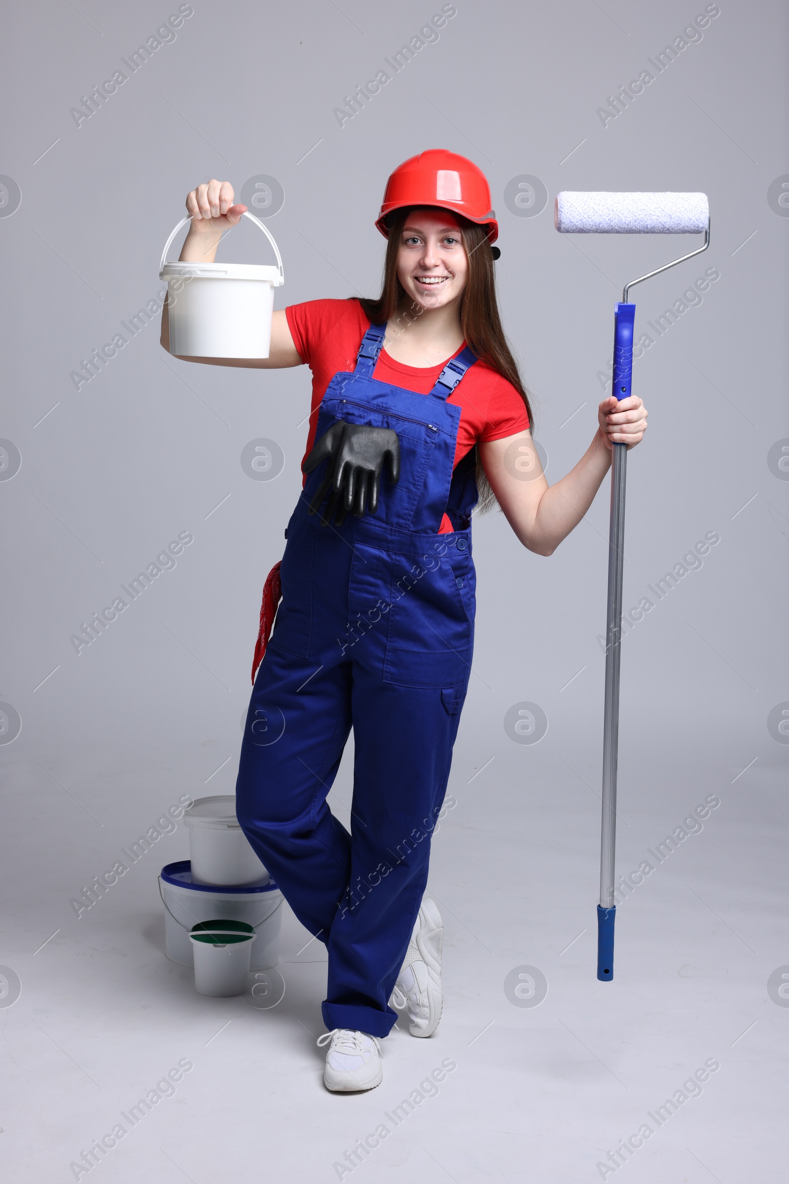 Photo of Professional painter with roller and buckets of paint on light grey background