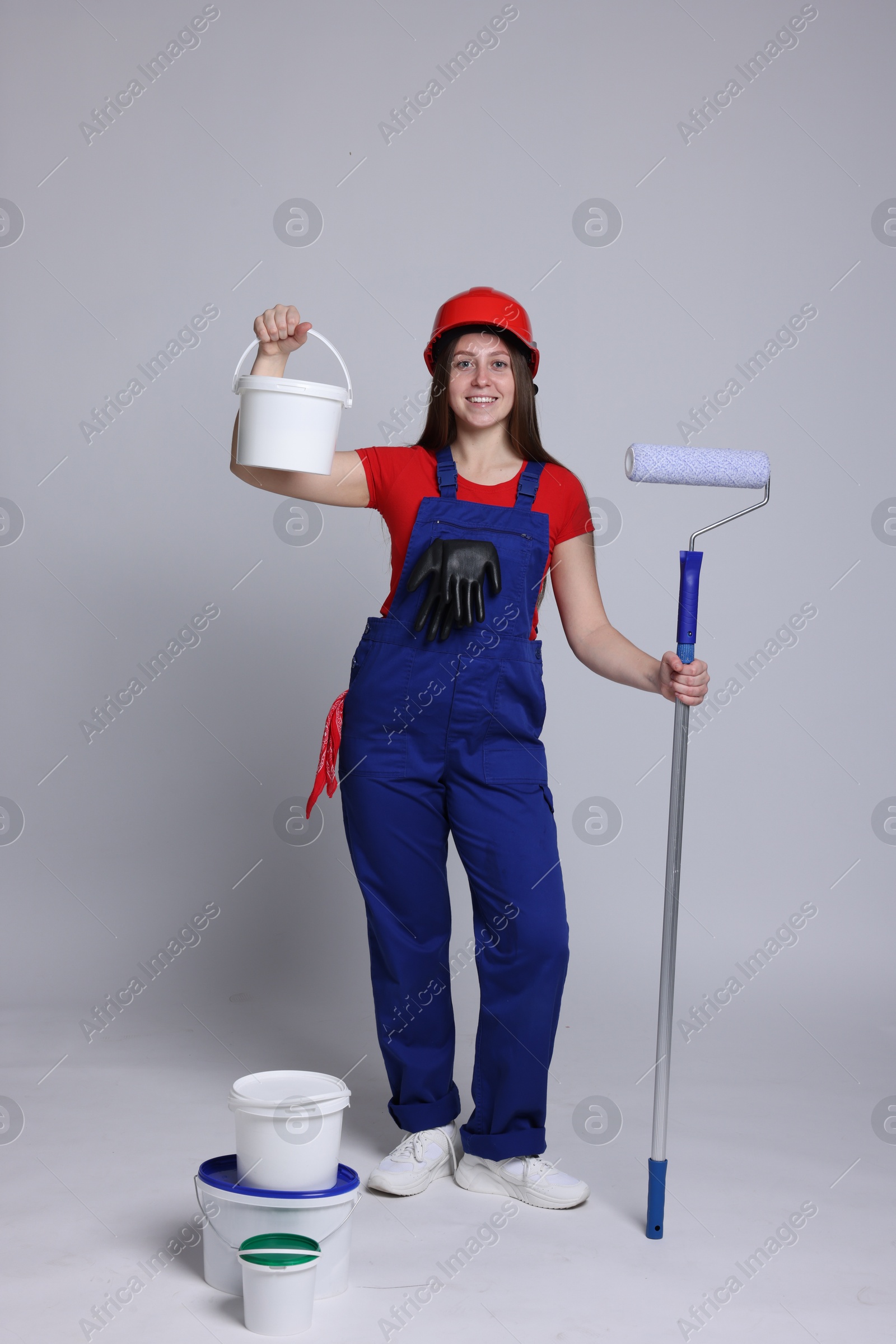 Photo of Professional painter with roller and buckets of paint on light grey background