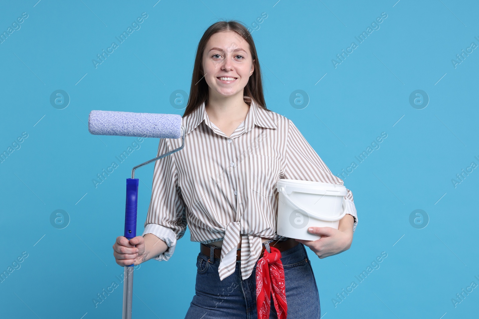 Photo of Woman with roller and bucket of paint on light blue background