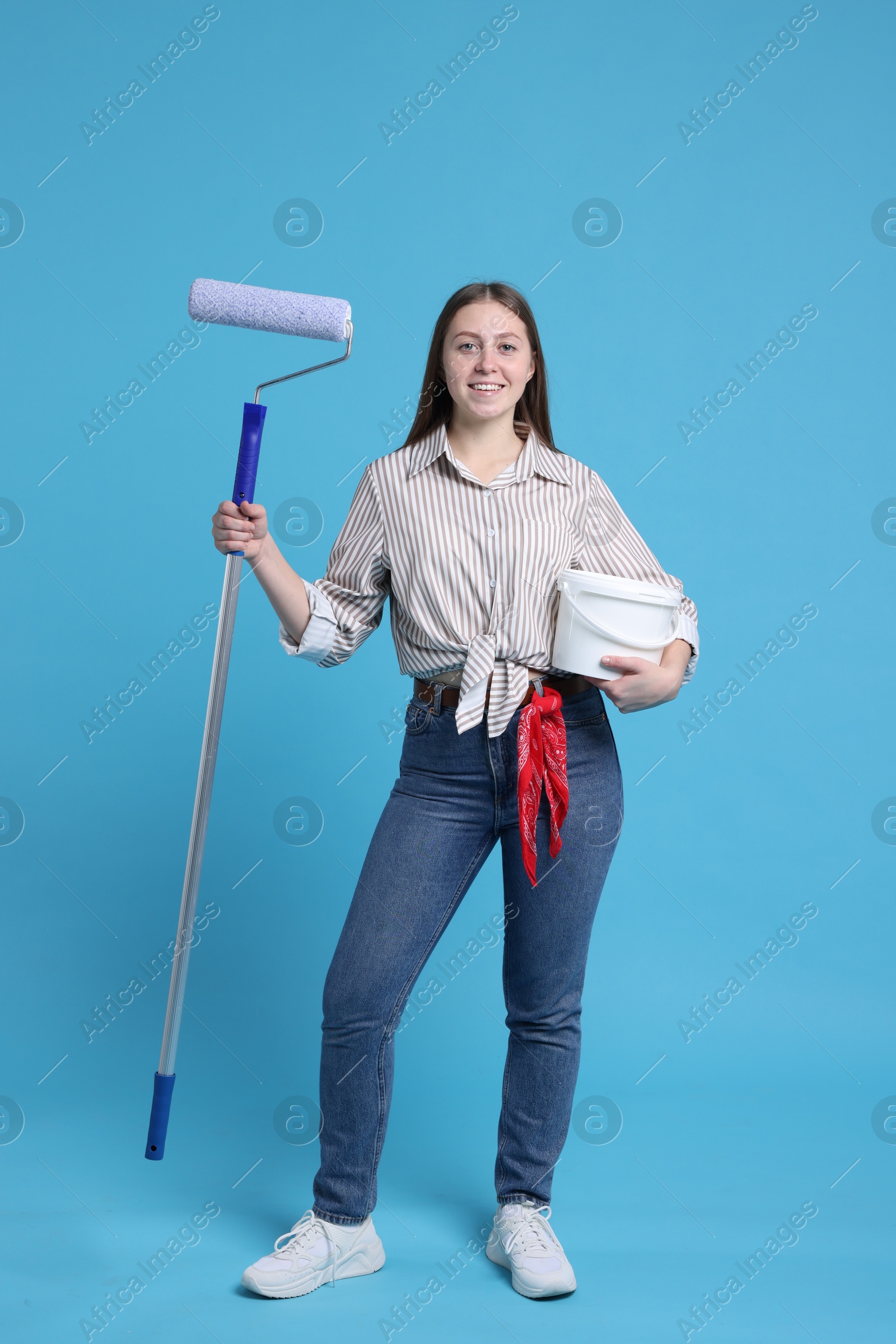 Photo of Woman with roller and bucket of paint on light blue background