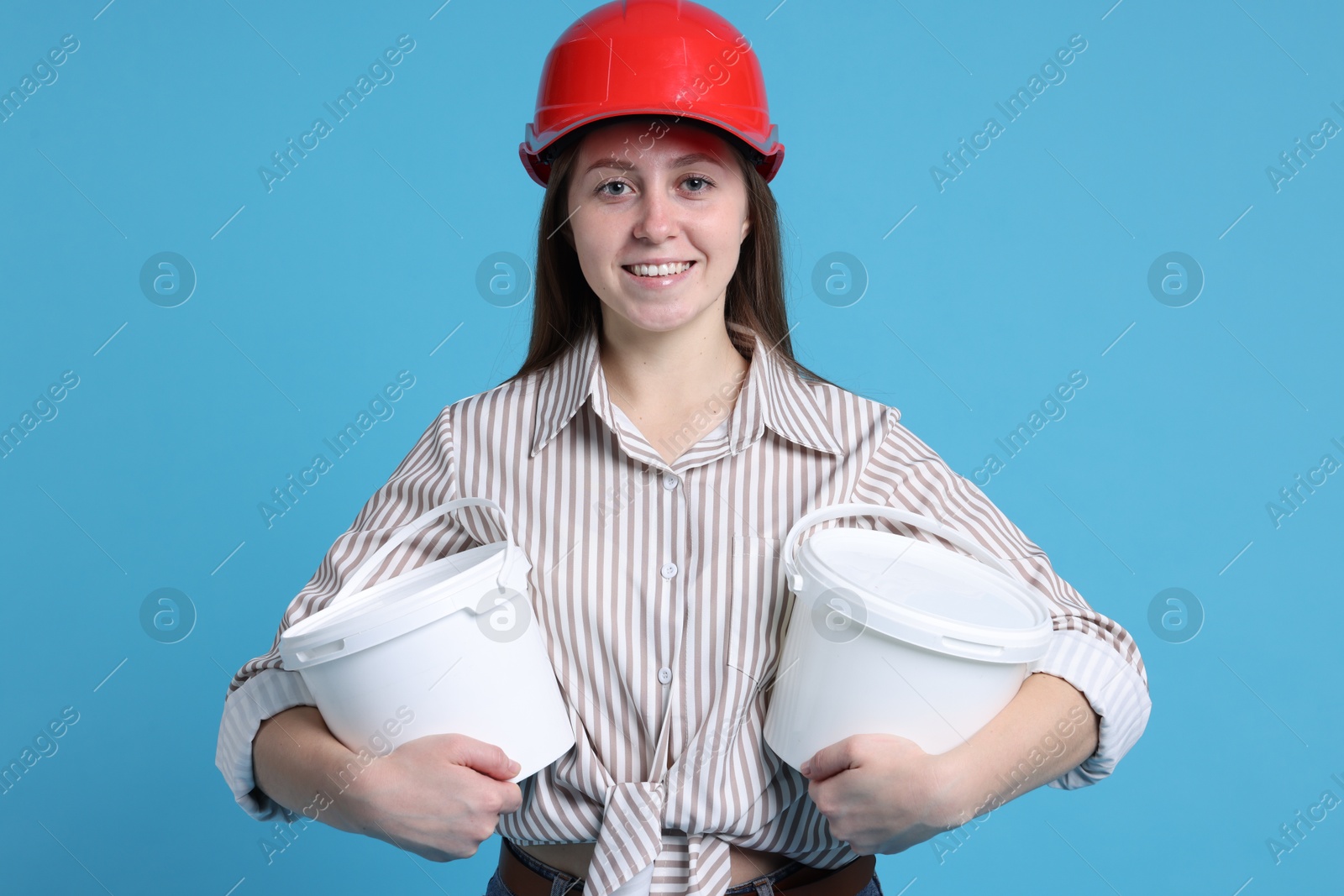 Photo of Woman wearing hardhat with buckets of paint on light blue background