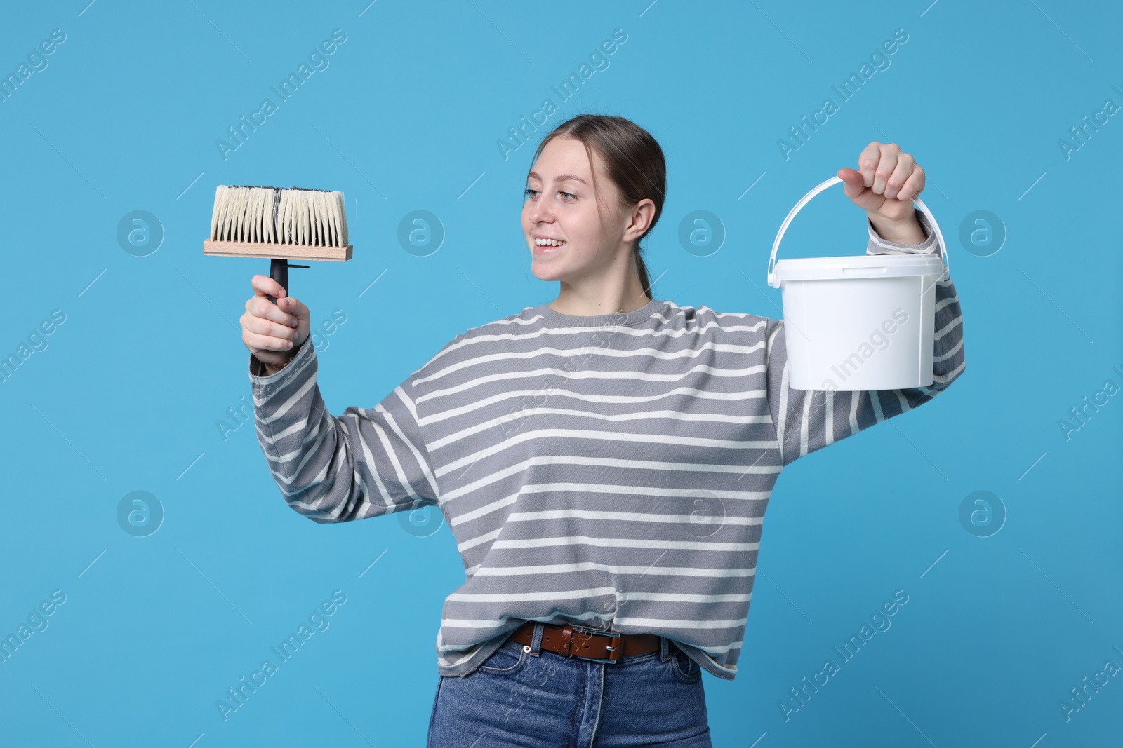 Photo of Woman with brush and bucket of paint on light blue background