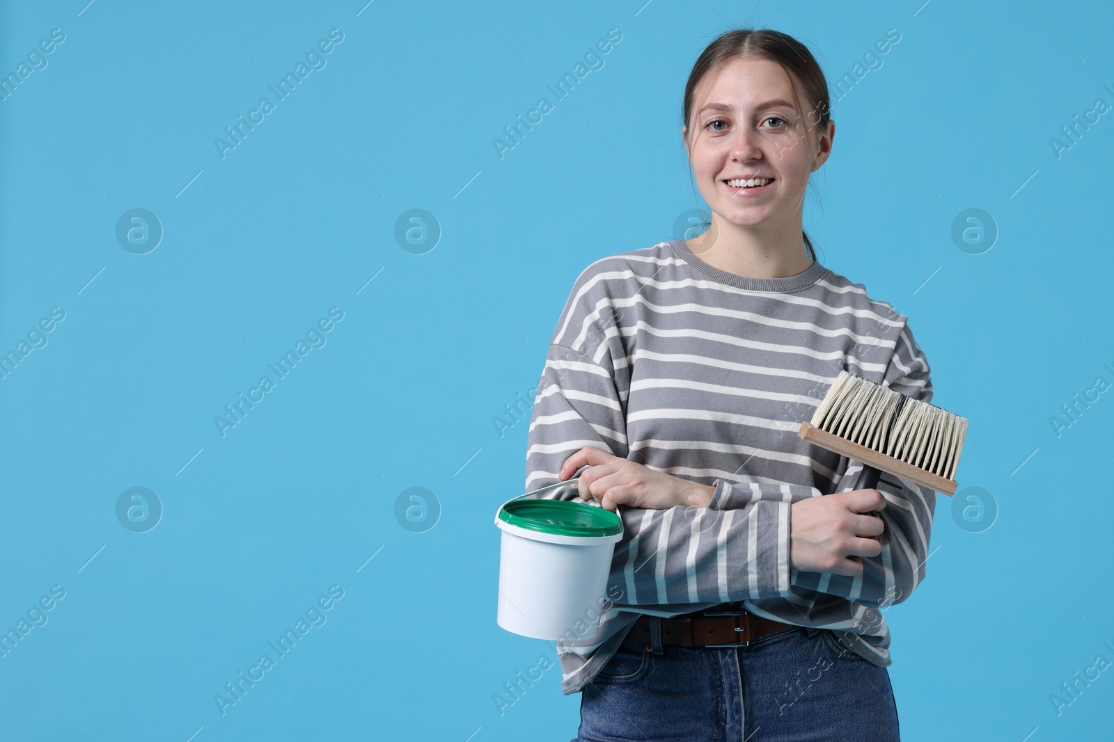 Photo of Woman with brush and bucket of paint on light blue background. Space for text