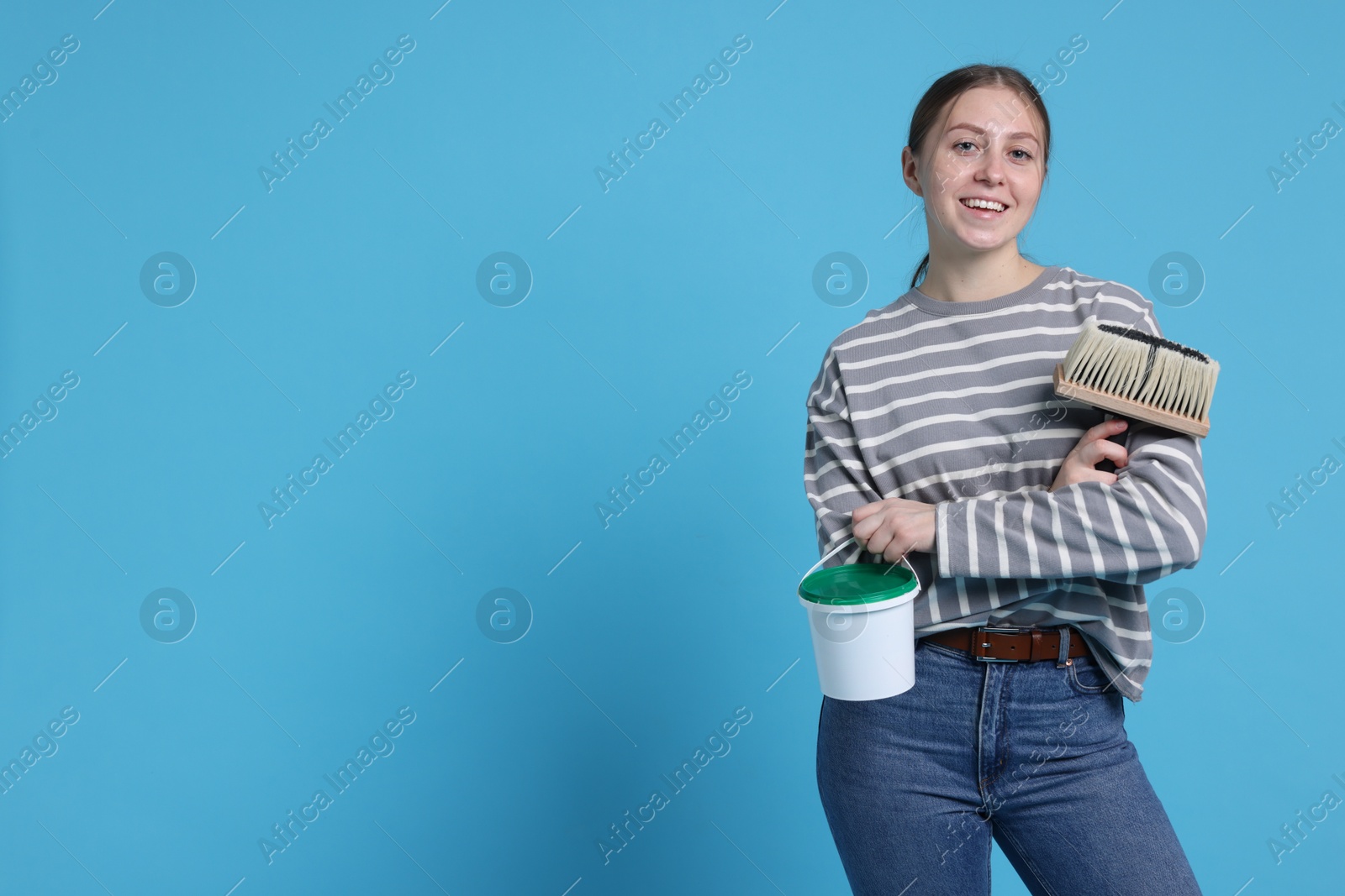 Photo of Woman with brush and bucket of paint on light blue background. Space for text