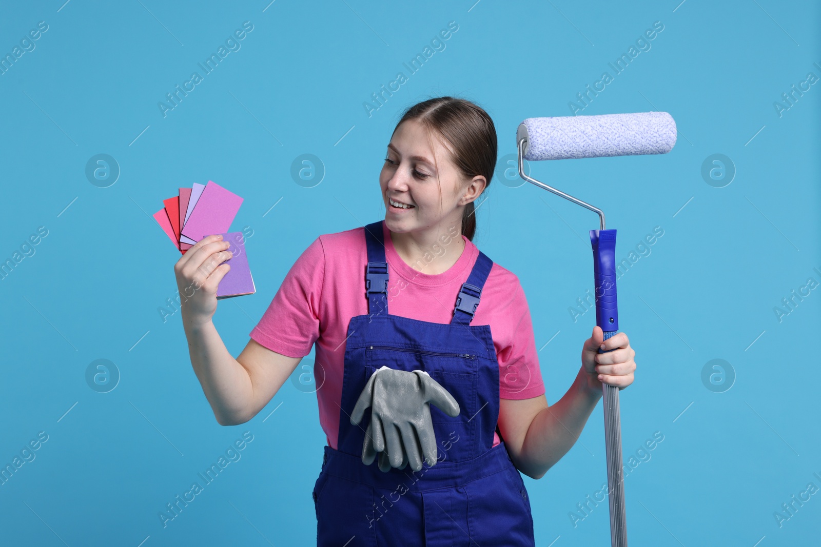 Photo of Professional painter with roller and color samples on light blue background