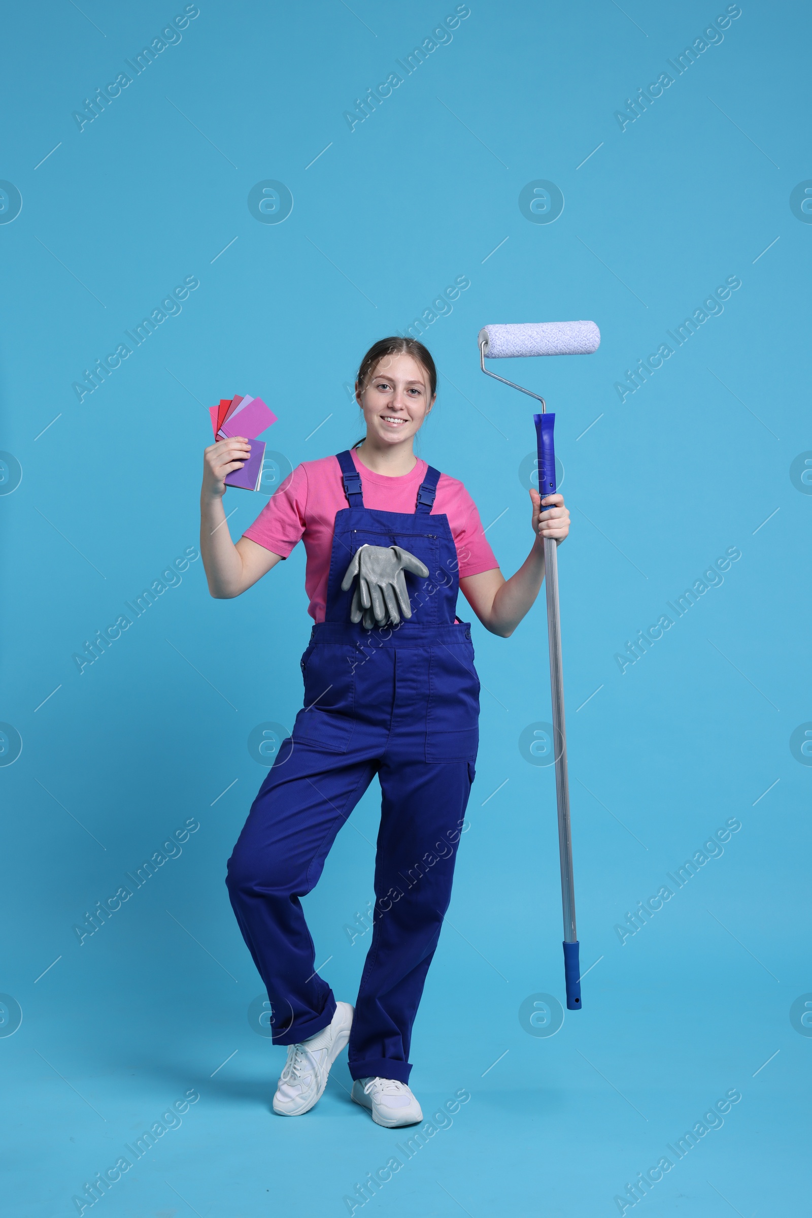 Photo of Professional painter with roller and color samples on light blue background