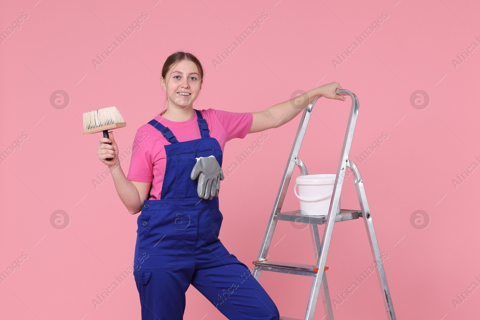 Photo of Professional painter with brush, bucket of paint and ladder on light pink background