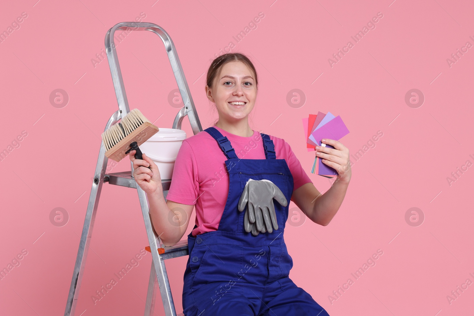 Photo of Professional painter with brush, color samples, bucket of paint and ladder on light pink background