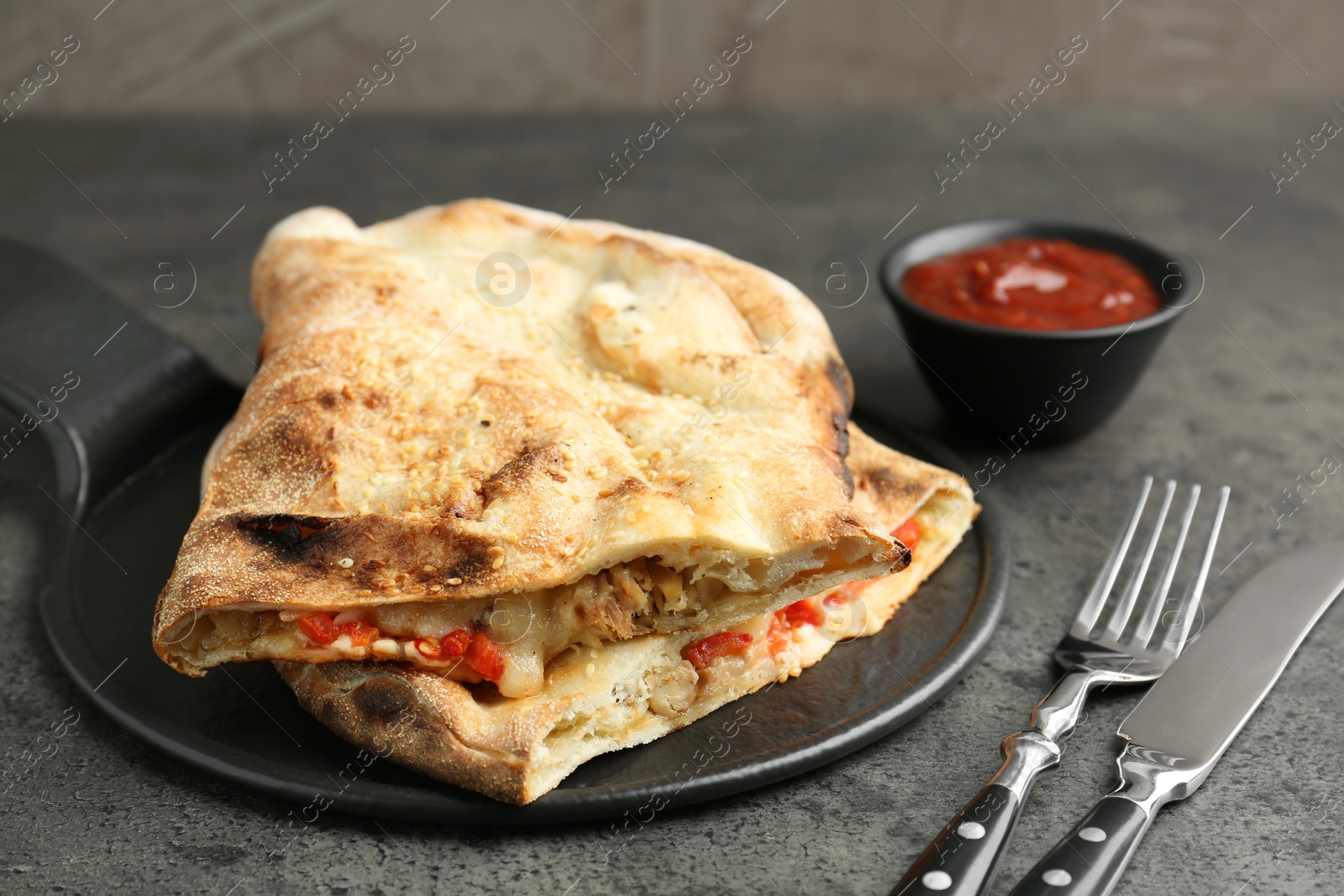 Photo of Halves of tasty calzone with meat, cheese, tomato and sauce on grey textured table, closeup