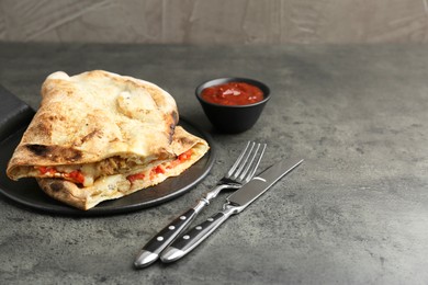 Photo of Halves of tasty calzone with meat, cheese, tomato and sauce on grey textured table. Space for text