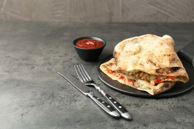 Photo of Halves of tasty calzone with meat, cheese, tomato and sauce on grey textured table. Space for text