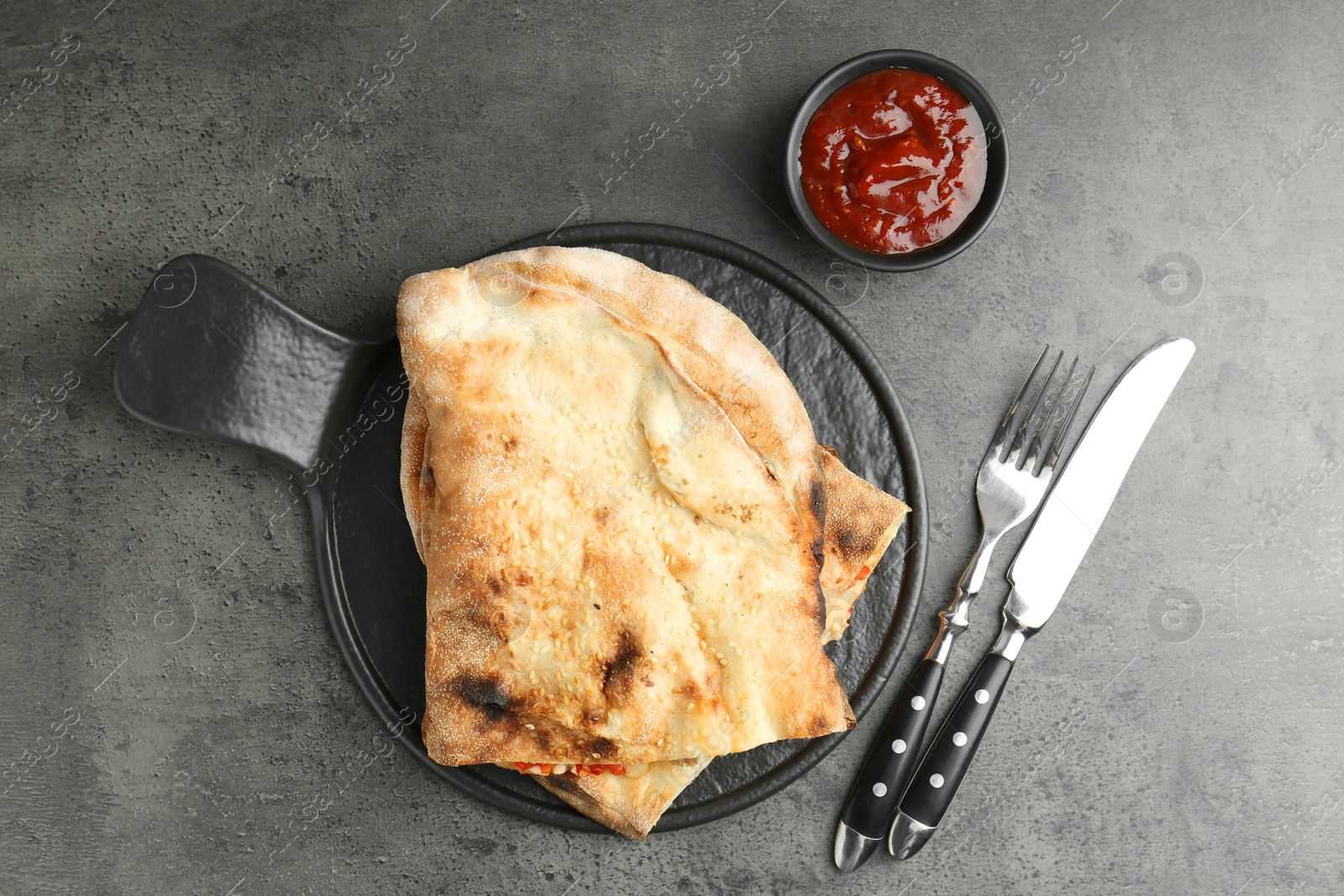 Photo of Halves of tasty calzone served with sauce on grey textured table, flat lay