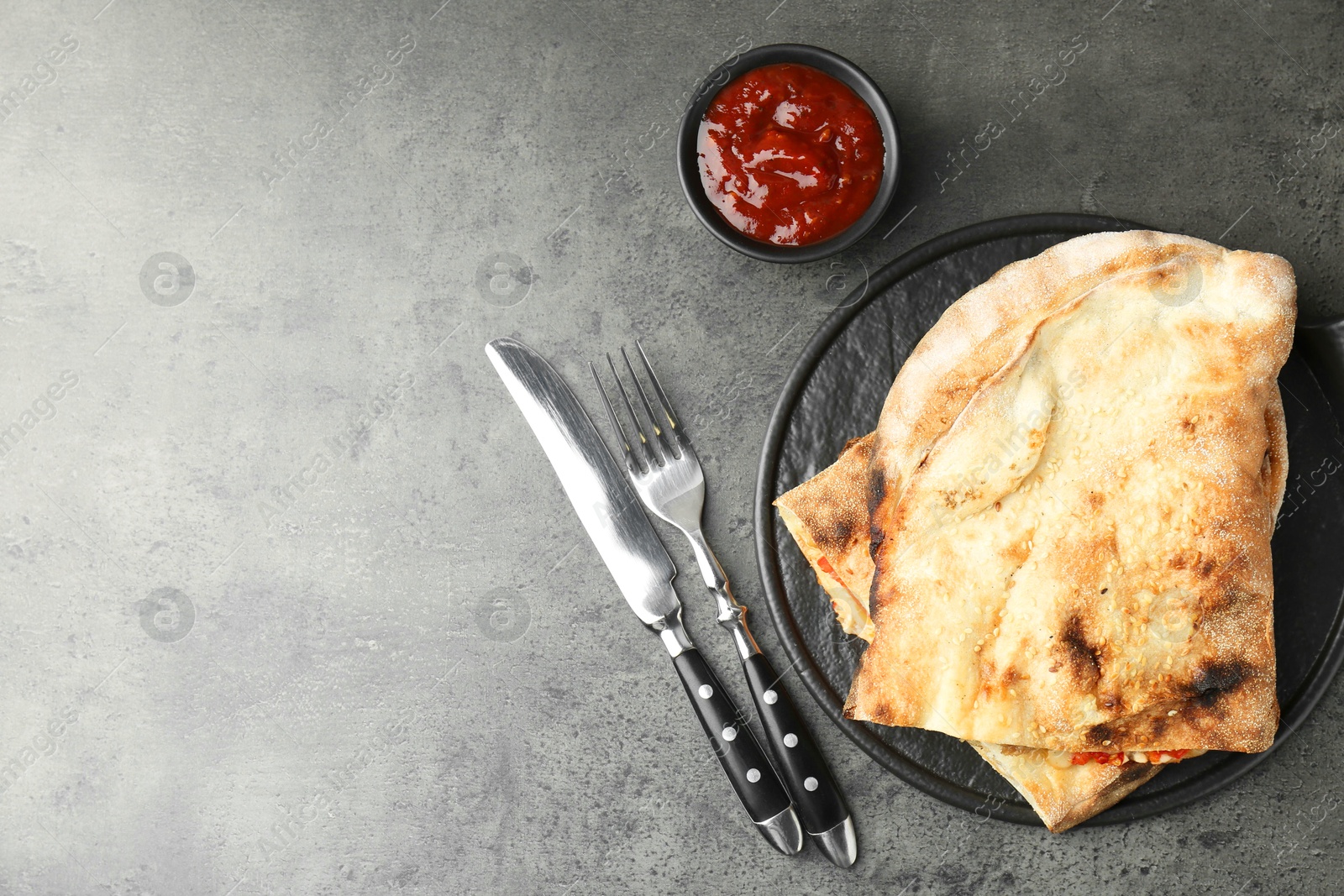 Photo of Halves of tasty calzone served with sauce on grey textured table, flat lay. Space for text