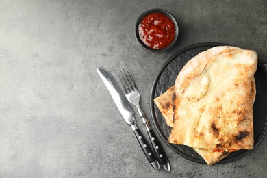 Photo of Halves of tasty calzone served with sauce on grey textured table, flat lay. Space for text