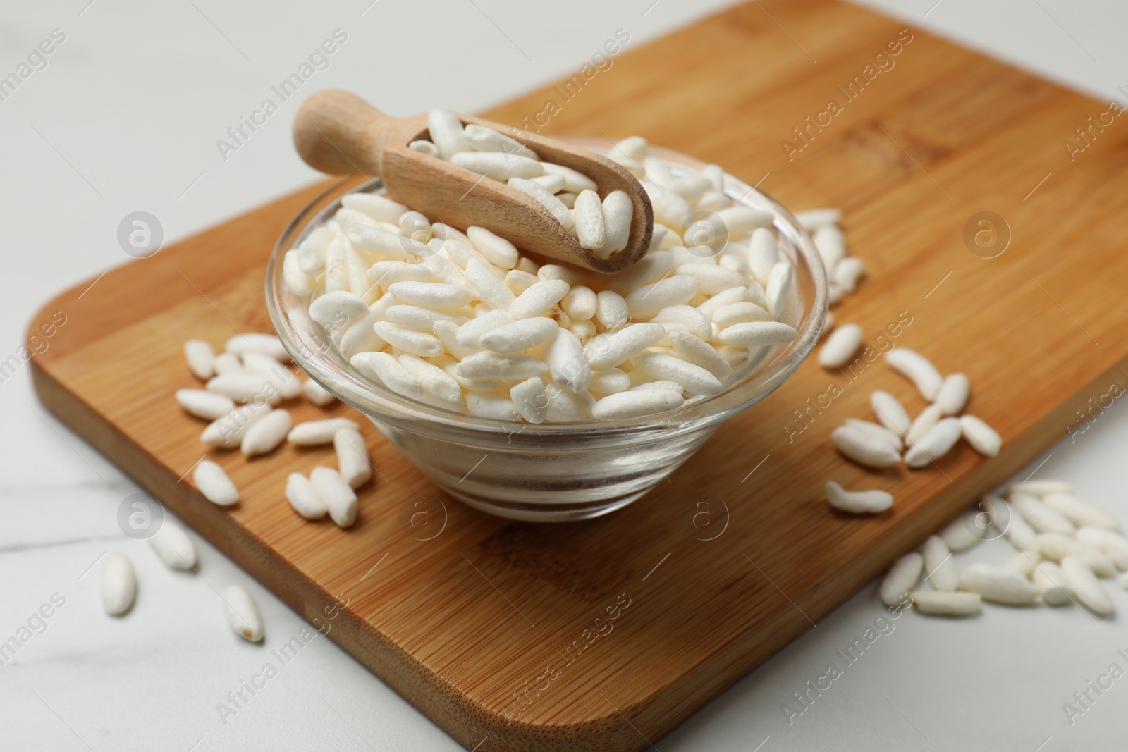 Photo of Puffed rice in bowl and scoop on white marble table, closeup