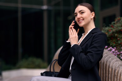 Photo of Woman in stylish formal suit talking on phone outdoors. Space for text