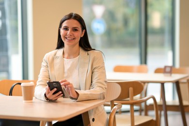 Photo of Woman in stylish formal suit with phone and coffee at table indoors. Space for text