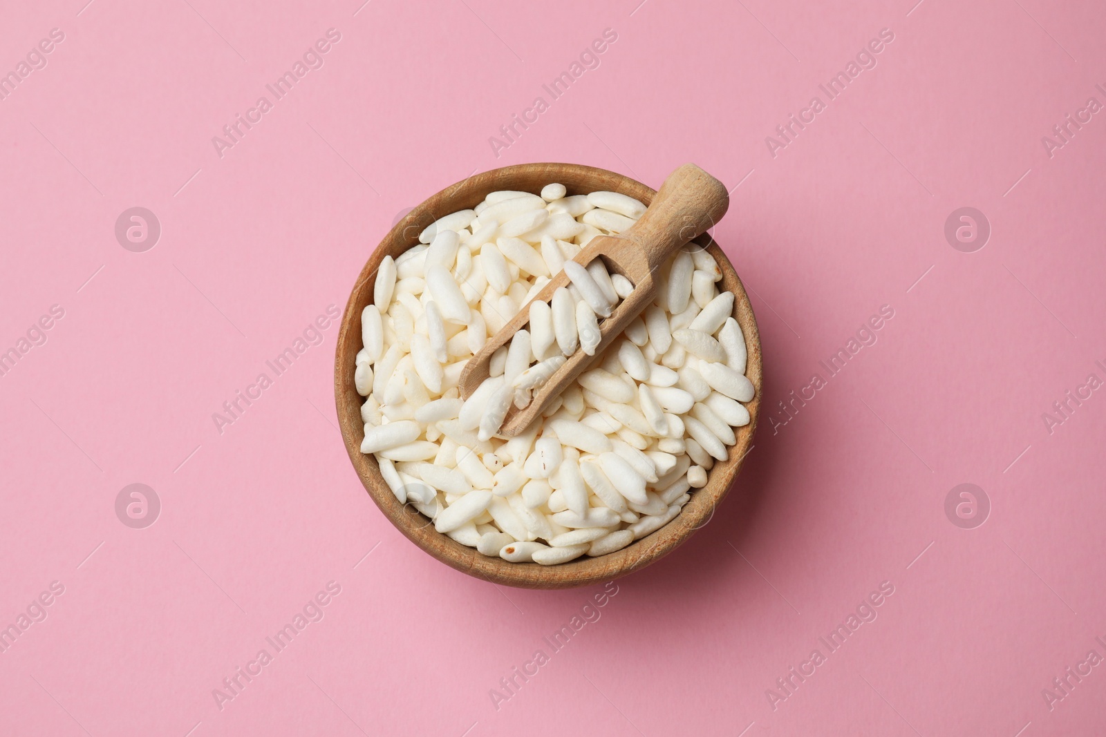 Photo of Puffed rice in bowl and scoop on light pink background, top view