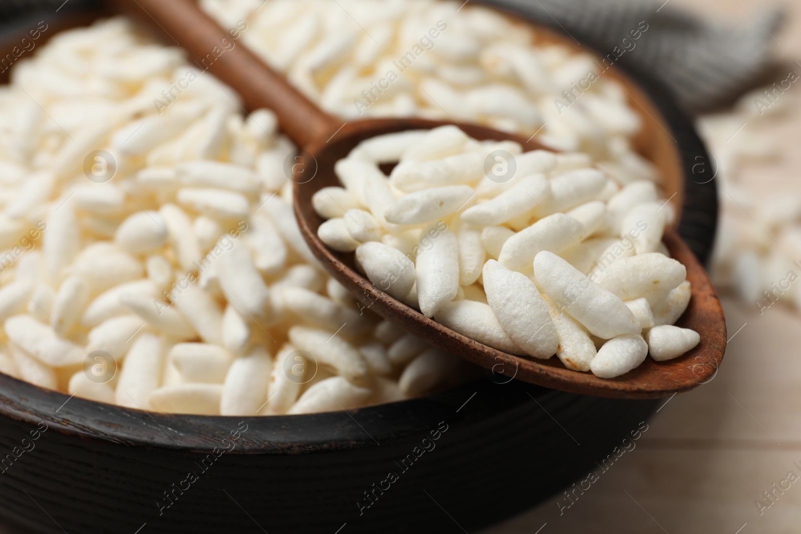 Photo of Puffed rice in bowl and spoon on white wooden table, closeup