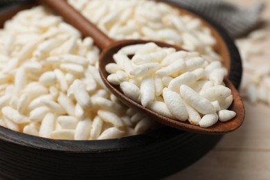 Photo of Puffed rice in bowl and spoon on white wooden table, closeup