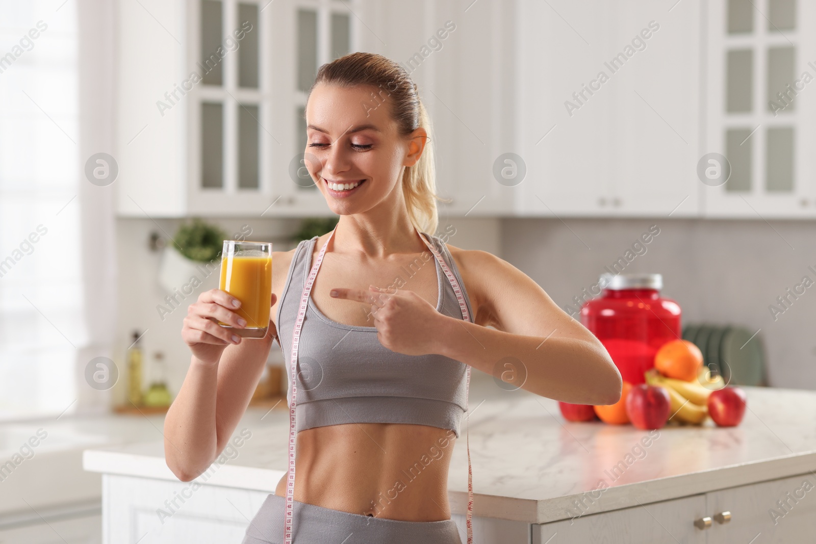 Photo of Weight loss. Happy woman with tasty shake and measuring tape in kitchen